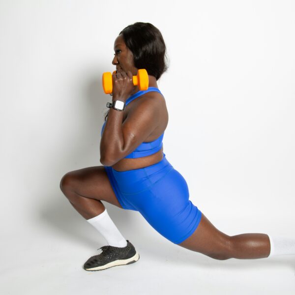 Woman in blue workout clothing lifting orange dumbbell