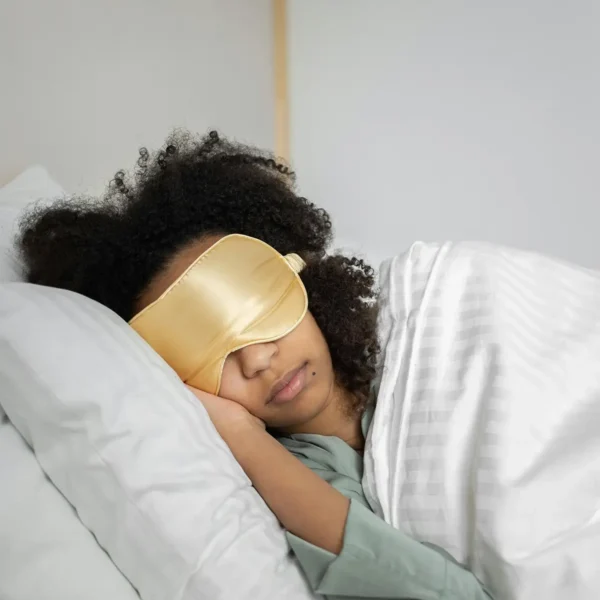 Woman laying in bed with sleep mask for article on connection between sleep and blood sugar
