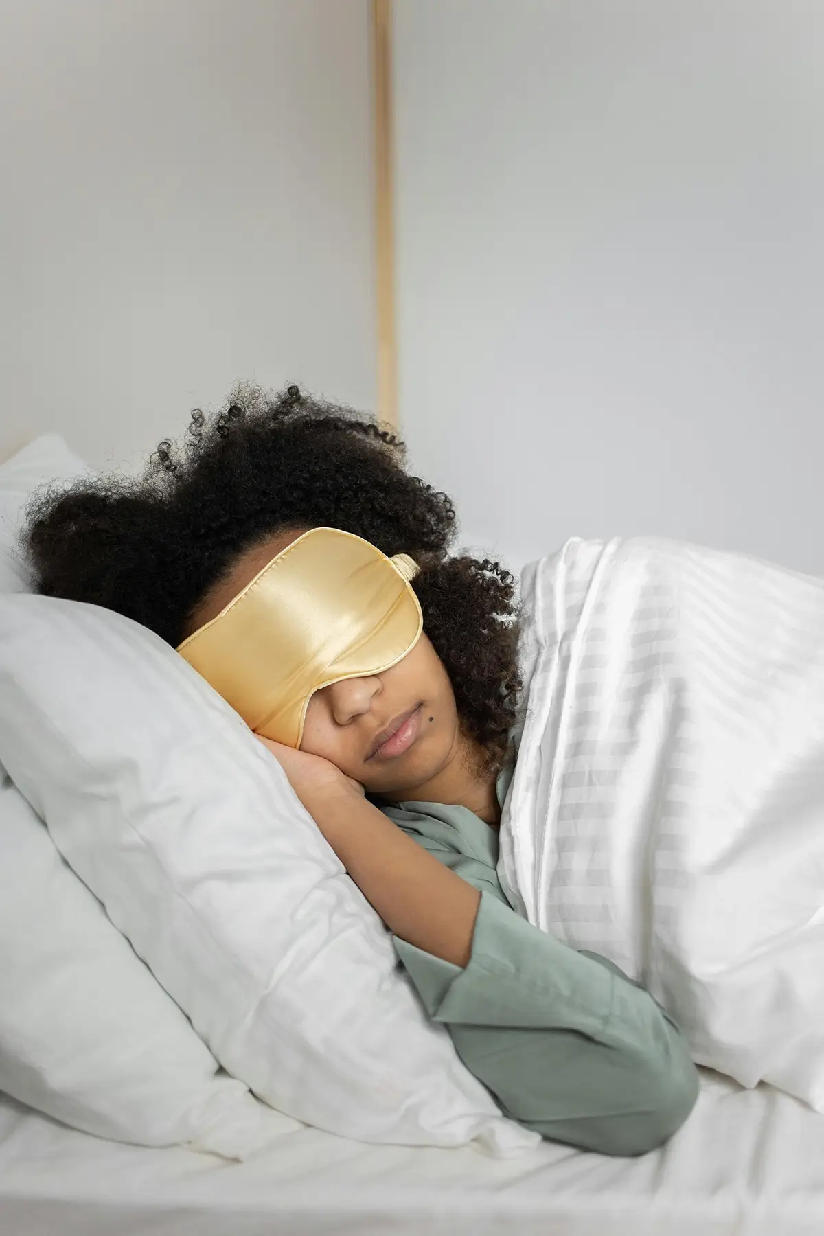 Woman laying in bed with sleep mask for article on connection between sleep and blood sugar